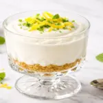 Taça de mousse de limão com biscoito triturado, raspas e uma rodela de limão.