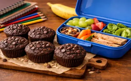 Muffins de cacau e aveia em forminhas coloridas ao lado de uma lancheira escolar.