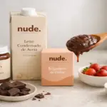 "Fotografia estilo editorial em uma bancada de cozinha moderna, mostrando as embalagens minimalistas da marca Nude (Creme de Aveia e Leite Condensado) ao lado de uma colher com brigadeiro cremoso feito à base de plantas."