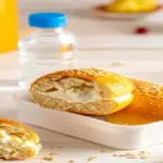 Lancheira escolar aberta com pães de queijo proteicos dourados, um deles aberto mostrando recheio de requeijão cremoso.